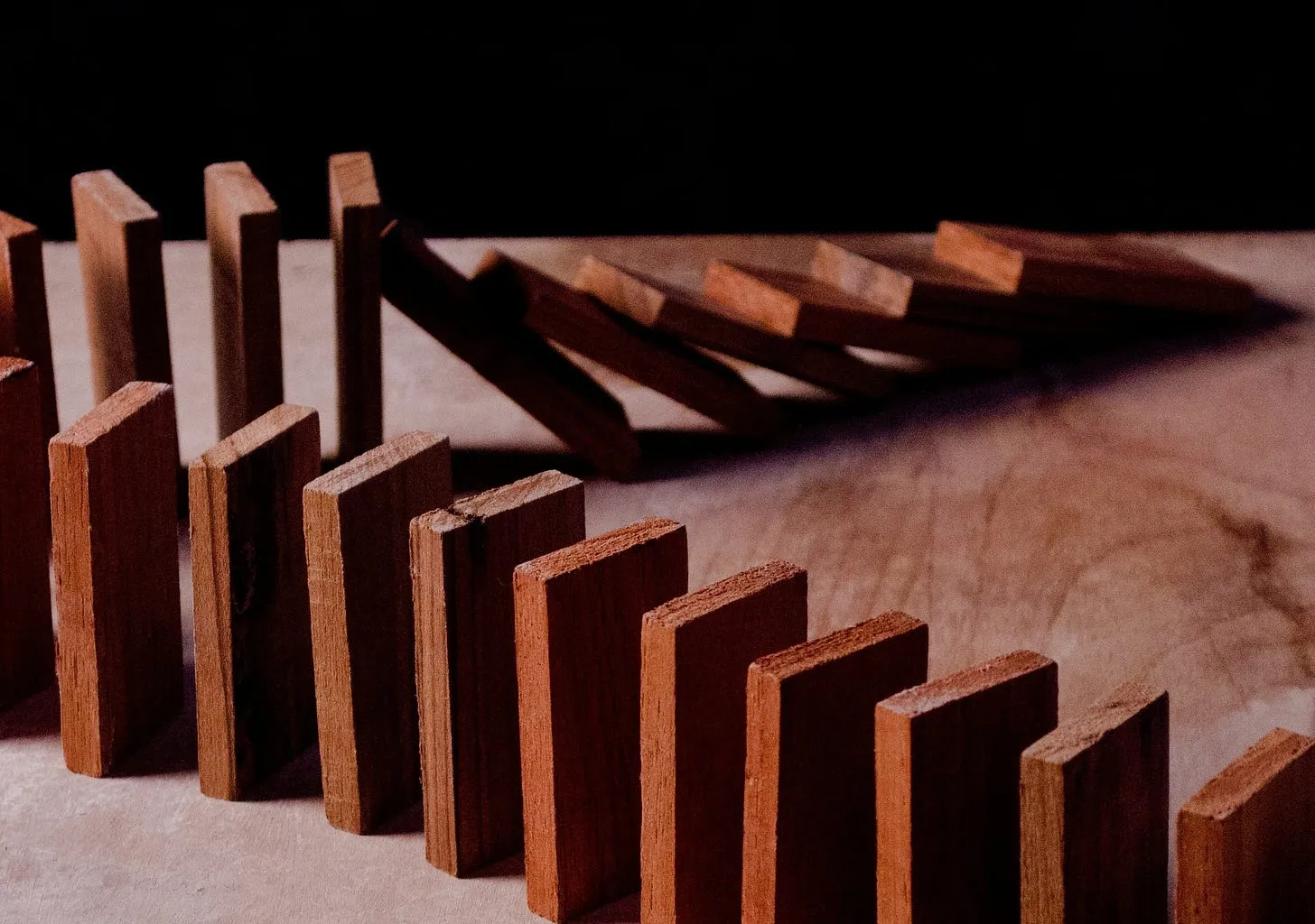 Wooden dominoes mid-cascade — a few still upright in front, the rest toppled behind.